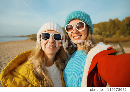 Happy young two women friends taking selfie with phone on beach, smiling girlfriends having fun 119378681
