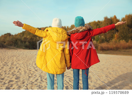 Back view happy joyful two women friends on sunny beach, stylish girlfriends together on sea coast Back view happy joyful two women friends on sunny beach, stylish girlfriends together on sea coast 119378689