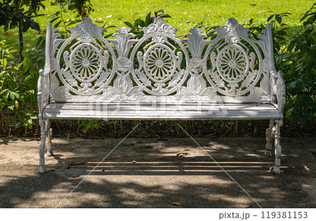 Sunlight on backrest surface of Empty ornate antique cast iron bench in a shady area of the quiet park area. 119381153