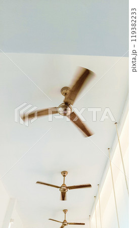 Fan at white ceiling spinning around to give some air at the room Fan at white ceiling spinning around to give some air at the room 119382233