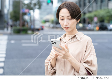 ビル街でスマートフォンを操作している女性 ビル街でスマートフォンを操作している女性 119382468
