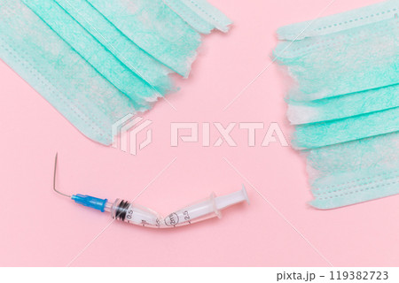 Broken Medical Syringe and Torn Medical Face Mask on the Pink Background Broken Medical Syringe and Torn Medical Face Mask on the Pink Background 119382723