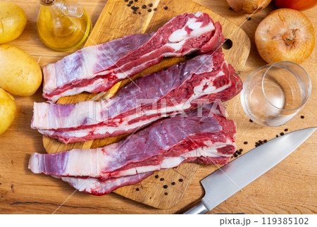 Raw beef ribs on board, potato tubers and whole onions 119385102