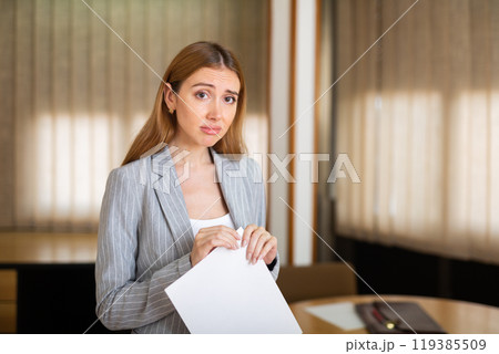 Upset young female office employee holding paper document Upset young female office employee holding paper document 119385509