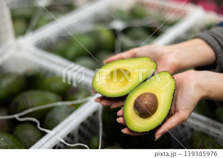Fresh ripe sliced avocado on hand, blurred boxes with fruits 119385976