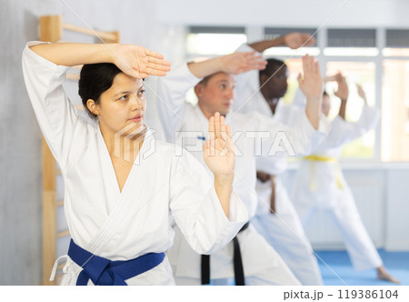 Middle-aged woman attendee of karate classes practicing kata standing in row with others 119386104