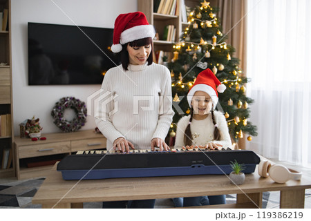 Mother and daughter play piano and sing Christmas carols together 119386219