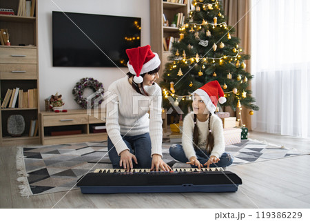 Mother and daughter play piano and sing Christmas songs at home 119386229