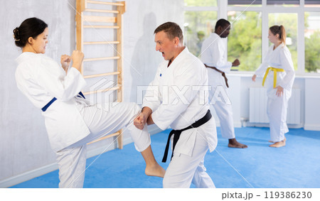 Middle-aged man attendee of karate classes fighting with his opponent in sports hall 119386230