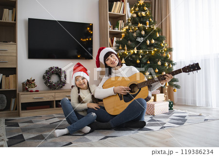 Mother and daughter enjoy Christmas music together at home 119386234