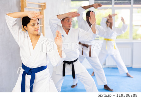 Women and men in kimono in fight stance during group karate training 119386289