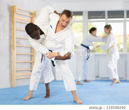 Two males practicing judo together on sports mats under the guidance of trainer 119386292