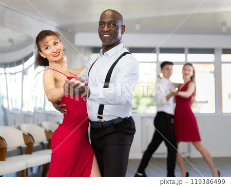 Smiling African American man dancing waltz with woman in red in studio Smiling African American man dancing waltz with woman in red in studio 119386499