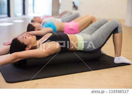 Group of people performs an exercise by placing a roll of a sports mat under their back 119386527