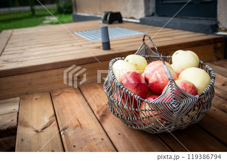 Wicker metal basket with ripe apples on the wooden terrace Wicker metal basket with ripe apples on the wooden terrace 119386794