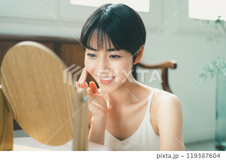 木製の卓上ミラーを見てスキンケアをする女性 木製の卓上ミラーを見てスキンケアをする女性 119387604