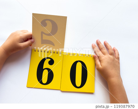 Childs hands flip through yellow pages with numbers. Displaying number 60 on white background Childs hands flip through yellow pages with numbers. Displaying number 60 on white background 119387970