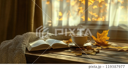 Cozy autumn scene with warm blanket, steaming cup, and open book by sunlit window 119387977