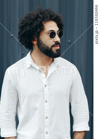 Arabian man with afro hairstyle and beard in white shirt standing at metal profile wall 119388466