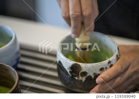 Woman whisking matcha powder while making matcha green tea with traditional accessories for tea ceremony 119389040