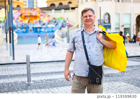 Happy adult man carrying shopping bag while walking cheerfully along city street Happy adult man carrying shopping bag while walking cheerfully along city street 119389630
