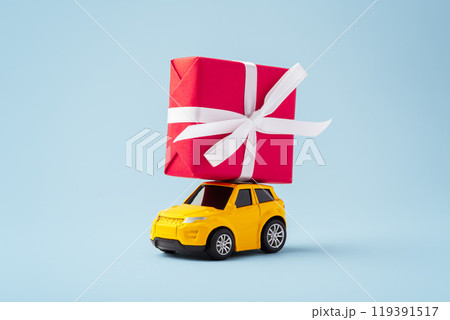 Car toy with red christmas gift box on the roof on blue background Car toy with red christmas gift box on the roof on blue background 119391517