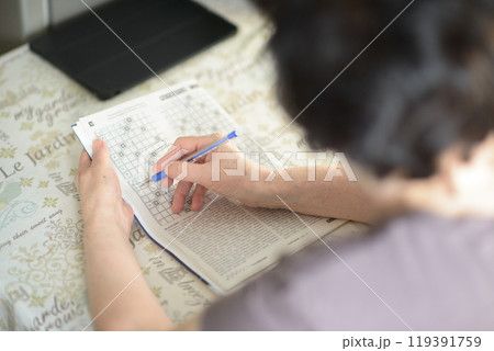 Senior Woman Solving Crossword Puzzle at Home with Tablet in Background 119391759