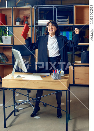 Emotional young woman in formal wear standing in office and expressing pure excitement, symbolizing triumph in her business 119392298
