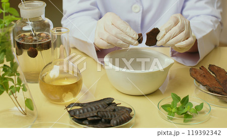 Herbal ingredients are placed on the table for the shampoo experiment while a scientist is conducting a shampoo experiment by breaking a brown dry herb into a white mortar. Herbal ingredients are placed on the table for the shampoo experiment while a scientist is conducting a shampoo experiment by breaking a brown dry herb into a white mortar. 119392342
