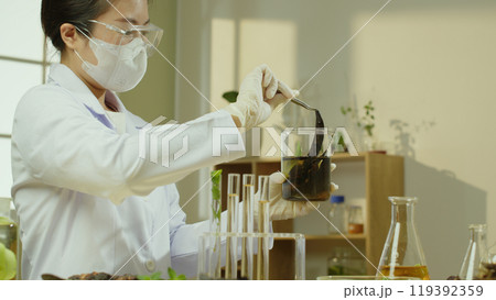 A horizontal lab image shows a researcher observing a soapberry that has been soaked in a beaker. The shelves and table in the background include supplies and ingredients for experiments. 119392359
