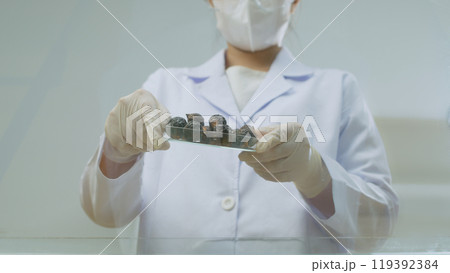 The photograph was shot from below view at scene of a researcher holding a glass tray of soapberry and prepare to pour it onto glass surface. Shampoo promotional pic, empty space to design 119392384