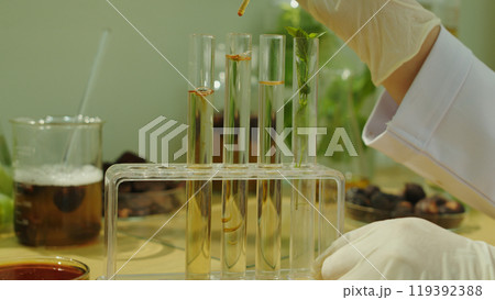 Close up shot from front view on experiment table, yellow extract from natural ingredient dropped into a glass test tube in rack. Advertising photo for natural shampoo product Close up shot from front view on experiment table, yellow extract from natural ingredient dropped into a glass test tube in rack. Advertising photo for natural shampoo product 119392388