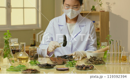 Female researcher conducting an experiment with natural ingredients on laboratory table for shampoo manufacturing. Front view photo, blank space for design 119392394