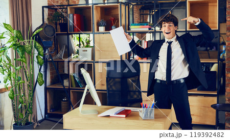 Successful deal. Happy young man, worker in formal wear standing in modern office and pointing at document, contract. New project Successful deal. Happy young man, worker in formal wear standing in modern office and pointing at document, contract. New project 119392482