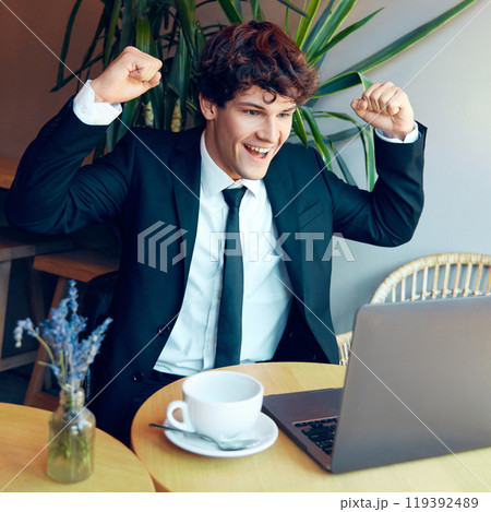 Young man in suit sitting at table with laptop and expressing happiness and excitement about successful project launch 119392489