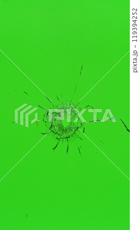 Close-up of gunshot through the glass, shattering against the green background 119394252