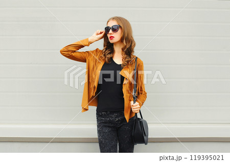 Fashion young woman wearing a sunglasses jacket black handbag posing on grey background 119395021
