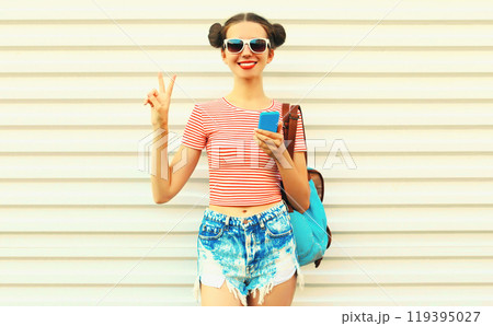 Portrait of happy smiling young woman with smartphone wearing a backpack on white background 119395027