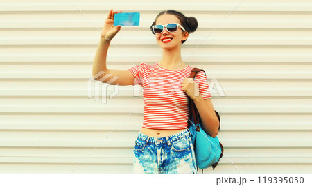 Portrait of happy smiling young woman taking selfie by smartphone with backpack on white background 119395030