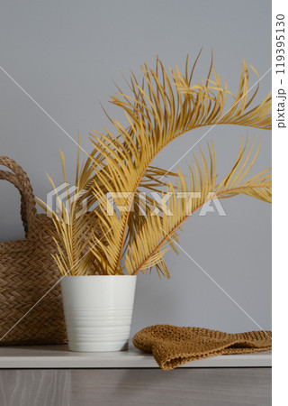 Fragment of a minimalist interior with a straw bag and hat in natural colors with palm branches. Summer vibes. Relaxed lifestyle on the coast. 119395130