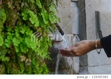 Female hands under a stream of water from a fountain. A fountain overgrown with plants. City fountain art. Female hands under a stream of water from a fountain. A fountain overgrown with plants. City fountain art. 119395365