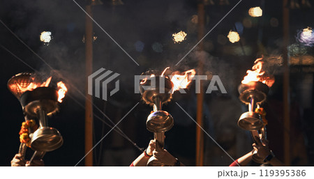 Varanasi, India. Man makes movements with a candle holder with lit candles on the Ganga Maha Aarti ceremony begins. Brahman priest wearing red and yellow dress doing traditional ganga aarti at ghat 119395386