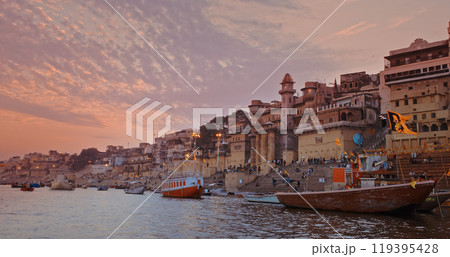 Varanasi, Uttar Pradesh, India. Cityscape Skyline In Evening Lights. Evening Pink Purple Sunset Sky, Dusk . Camera Moving Along Riverbank Embankment. Cinematic View From Boat Ride Past Darbhanga Ghat 119395428