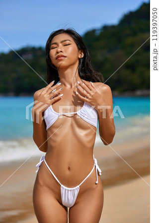 Beautiful asian girl in white bikini posing at the tropical beach. Close-up 119397050