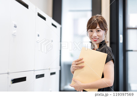 郵便受けの前で定形外郵便封筒を抱える女性 郵便受けの前で定形外郵便封筒を抱える女性 119397569