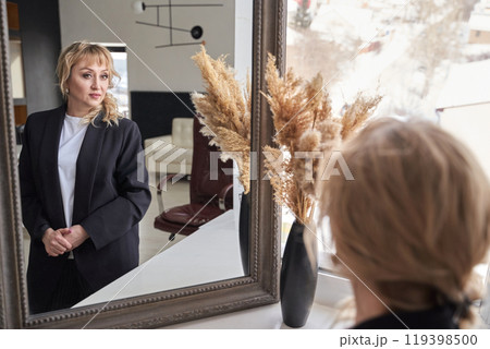 Woman in black blazer reflecting in mirror with modern interior and pampas grass Woman in black blazer reflecting in mirror with modern interior and pampas grass 119398500