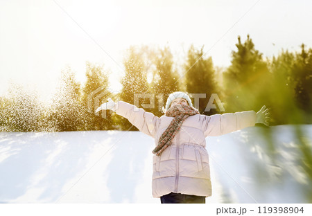 Happy beautiful child portrait. Excited kid playing in winter mountains forest. Funny little girl throwing snow into air, having fun. Snowy evergreen trees around ski resort. Christmas holiday vibes 119398904
