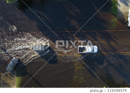 Flooded Florida road with evacuating cars and surrounded with water houses in suburban residential area. Consequences of hurricane natural disaster 119399574