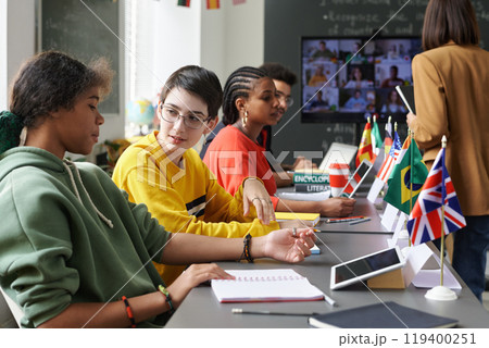 Multiethnic group of students sitting at table with country flags and communicating during international conference, copy space 119400251