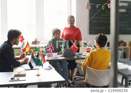 Diverse group of students sitting at table with flags during international conference in school classroom Diverse group of students sitting at table with flags during international conference in school classroom 119400256